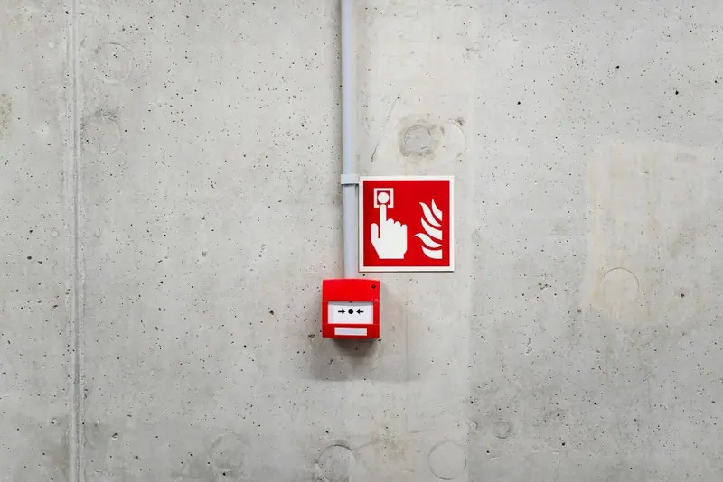 Red fire alarm manual call point on a concrete wall